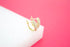 A pair of sparkling gold huggie hoop earrings encrusted with small crystals rests on a white block against a vibrant pink background.