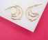 A pair of polished gold multi-strand hoop earrings featuring delicate knot accents rests on a white and bright pink surface.