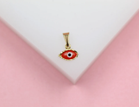 A small gold evil eye pendant with vibrant red enamel rests on a white display against a soft pink background.