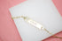 A delicate gold ID bracelet featuring the engraved word "LOVE" rests on a white display block against a pink background.