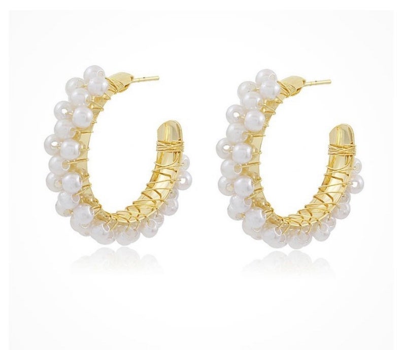 A pair of elegant gold hoop earrings embellished with delicate white pearls features intricate wire wrapping against a clean white background.