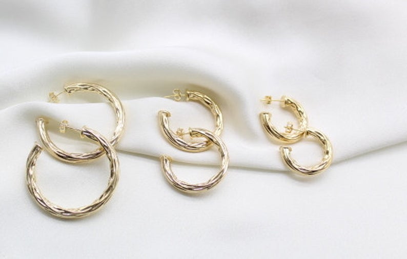 Three pairs of textured gold hoop earrings rest neatly on a soft white fabric background.
