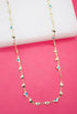 A delicate gold chain necklace drapes against a vibrant pink background, featuring alternating gold heart charms and tiny blue-and-white evil eye beads.
