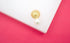 A chic gold double-sided earring featuring a textured textured gold sphere and a glossy white pearl rests on a white display against a vibrant pink background.