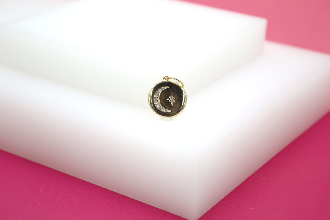 A gold crescent moon and star pendant sparkles against white and pink display blocks.