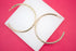 A pair of large, polished gold hoop earrings rests on a white display block against a vibrant pink background.