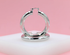 A pair of thick, polished silver hoop earrings rests on a white display block against a soft pink background.