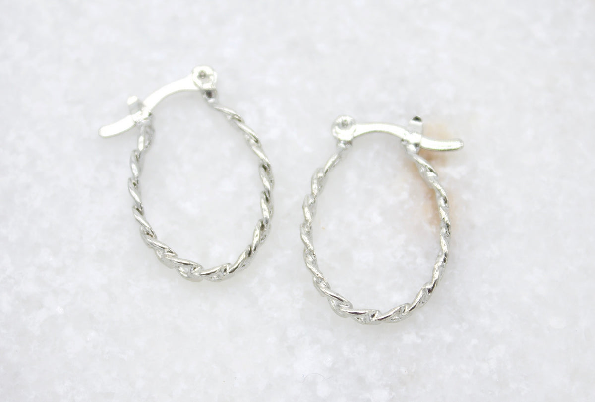 A pair of silver twist hoop earrings rests against a white textured surface.