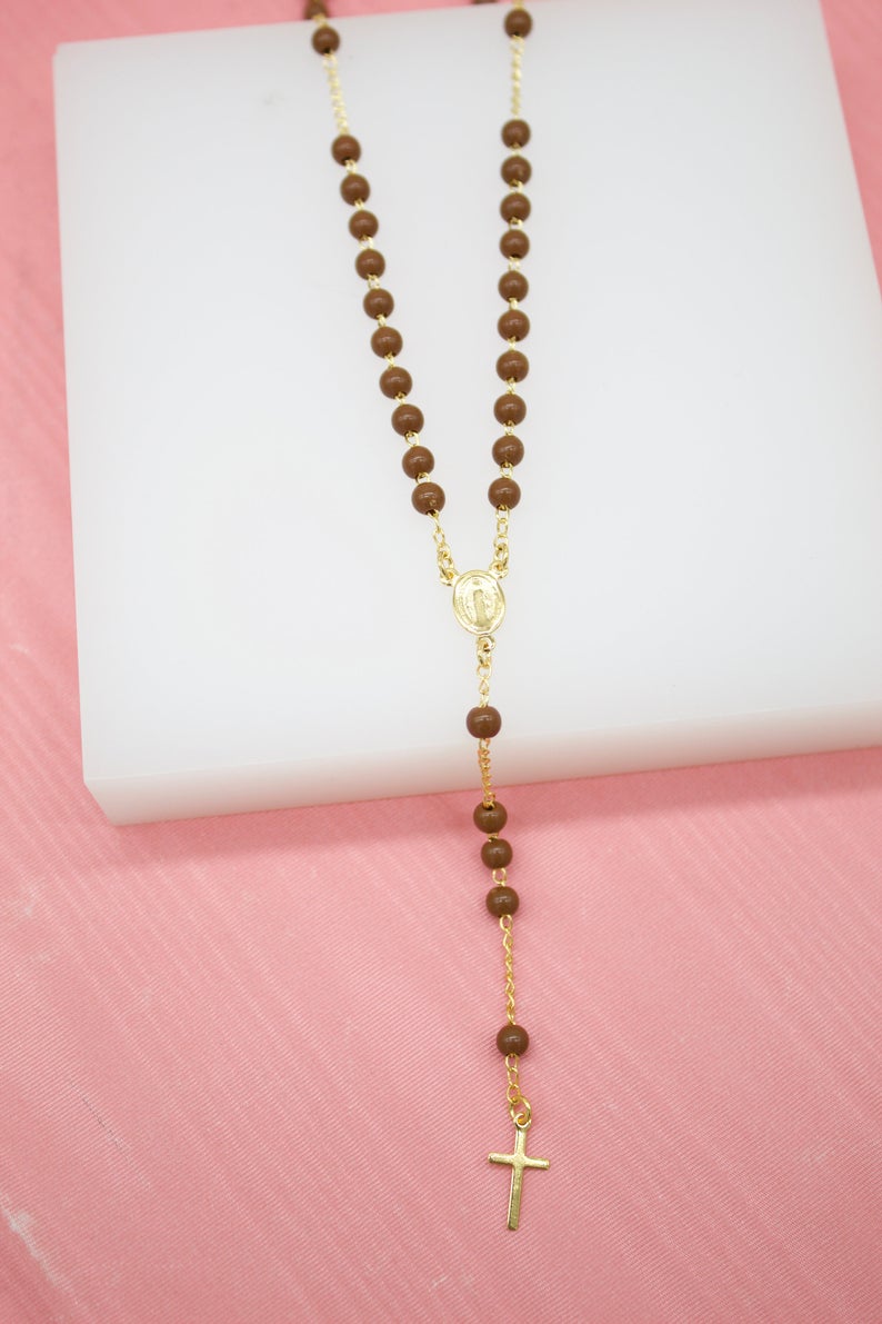 A catholic rosary necklace featuring smooth brown wooden beads and a delicate gold-plated crucifix rests on a white display surface.