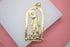 A gold San Lázaro pendant rests on a white display against a pink background, showcasing the intricate cutout figure of the saint accompanied by his dogs.