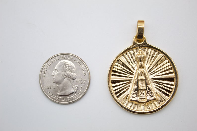 A round gold Our Lady of Aparecida pendant rests next to a US quarter coin to show its size.