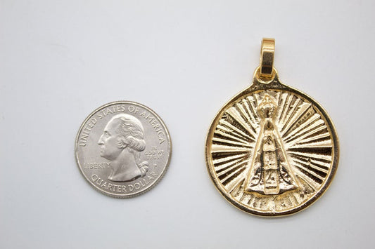 A round gold Our Lady of Aparecida pendant rests next to a US quarter coin to show its size.