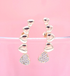A pair of gold heart-shaped crawler earrings sparkle against a soft pink background.