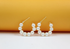A pair of gold hoop earrings adorned with alternating white pearls sits against a warm orange and white backdrop.