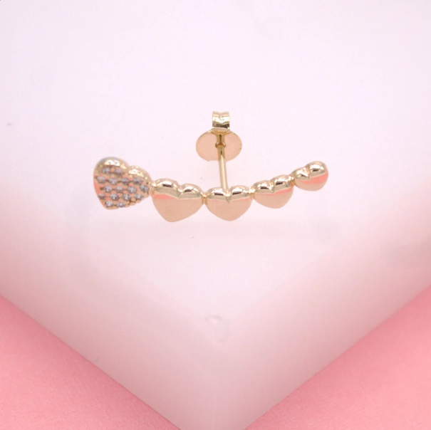 A delicate gold ear crawler earring features a row of graduated hearts, with the largest heart encrusted in sparkling pavé stones.