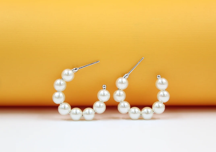 A pair of elegant faux pearl hoop earrings rests against a vibrant yellow backdrop.