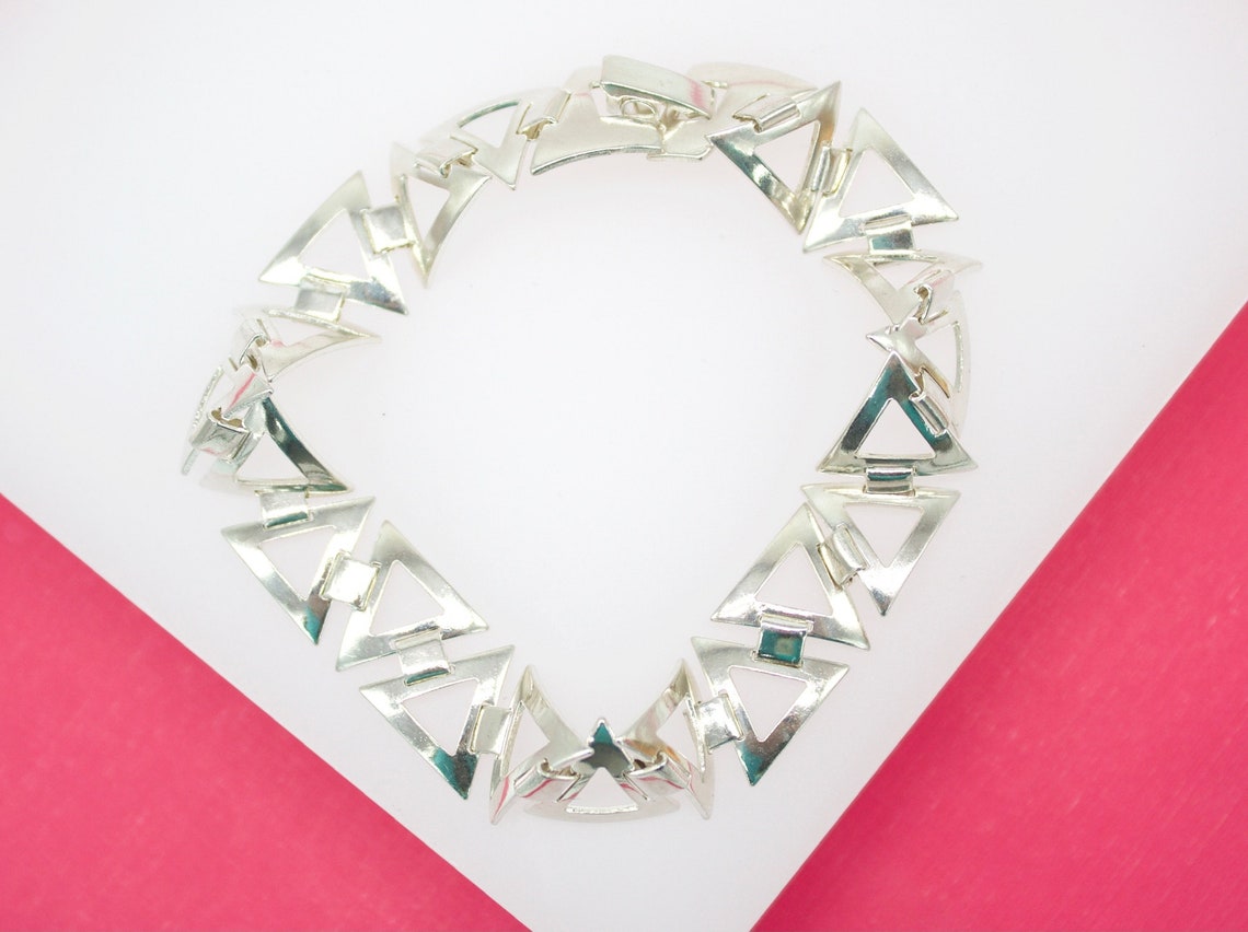 A silver link bracelet featuring geometric triangular shapes rests on a white and pink surface.
