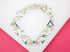 A silver link bracelet featuring geometric triangular shapes rests on a white and pink surface.