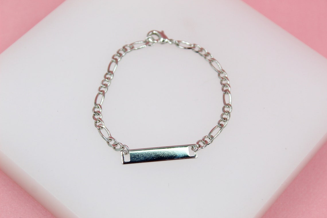 A shiny silver ID bracelet rests on a white display against a soft pink background.