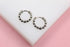 A pair of shiny silver beaded huggie hoop earrings rests on a white display stand against a pink background.