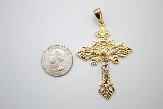 A detailed gold and silver crucifix pendant lies next to a US quarter coin for scale on a light gray surface.