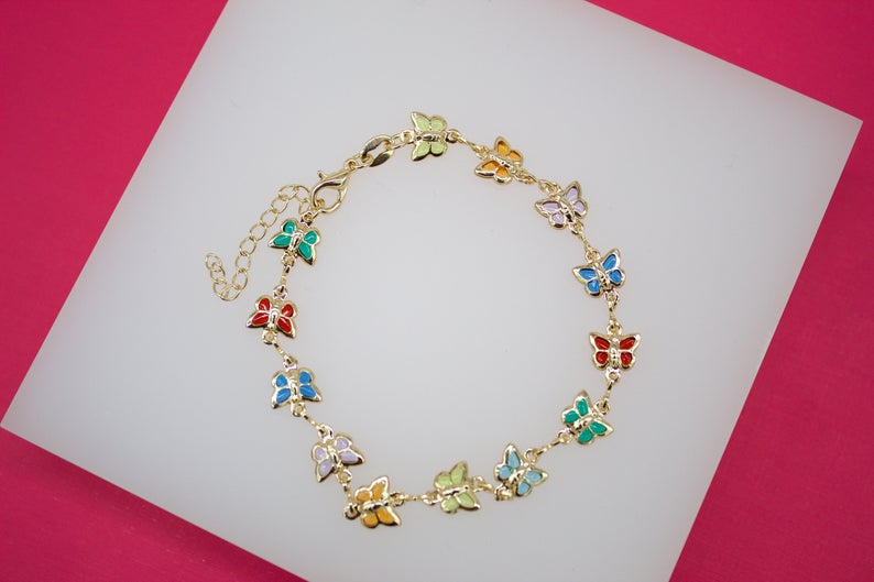 A gold butterfly charm bracelet displays colorful enamel butterflies in vibrant shades of red, blue, green, and yellow against a white display block.