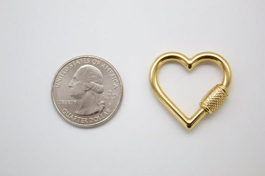 A shiny gold heart-shaped carabiner lies next to a US quarter coin on a light surface to show its size.
