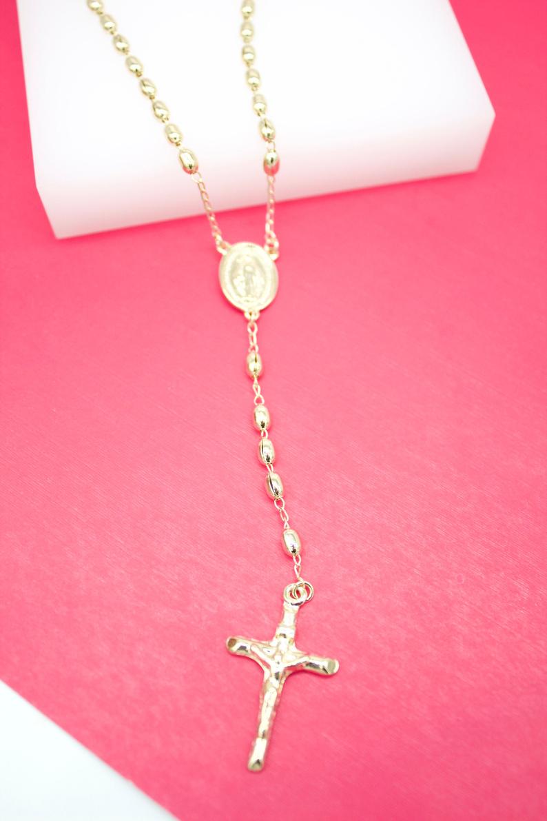 A shiny gold rosary necklace featuring oval beads and a crucifix rests against a vibrant pink and white background.