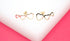 A pair of gold heart crawler earrings rests on a white display block against a vibrant pink background.
