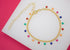 A gold chain charm bracelet dangles colorful enameled star pendants against a white and pink background.