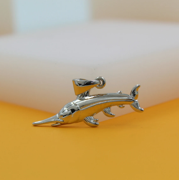 A polished silver swordfish pendant rests on an orange surface against a neutral background.