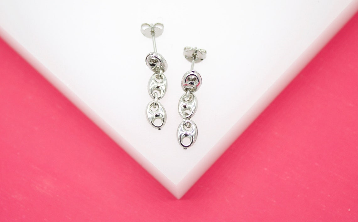 A pair of polished silver dangling chain-link earrings rests on a white and pink display stand.