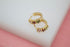 A pair of gold huggie hoop earrings with multicolored crystal stones rests on a white display surface.
