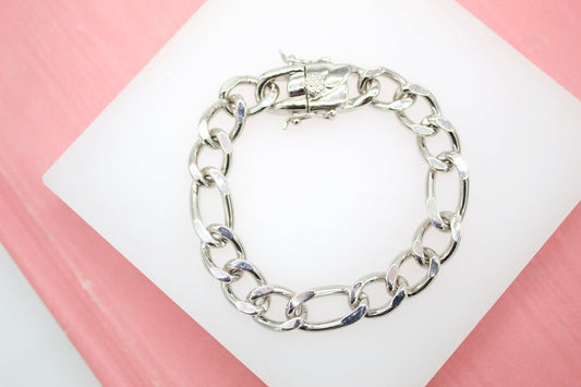 A chunky silver chain bracelet rests neatly on a white display pad against a soft pink background.