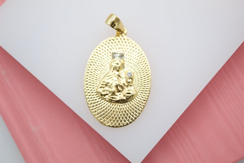 A gold oval pendant displays a textured depiction of the Virgin Mary with a sparkling diamond accent.