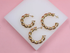 Three polished gold twist hoop earrings rest on a white display stand against a pink background.