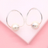 A pair of elegant silver hoop earrings featuring dangling white pearls rests against a soft pink backdrop.