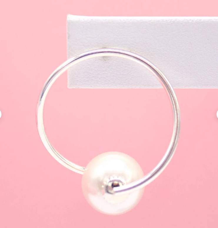A silver hoop earring holding a single white pearl hangs against a pink background.