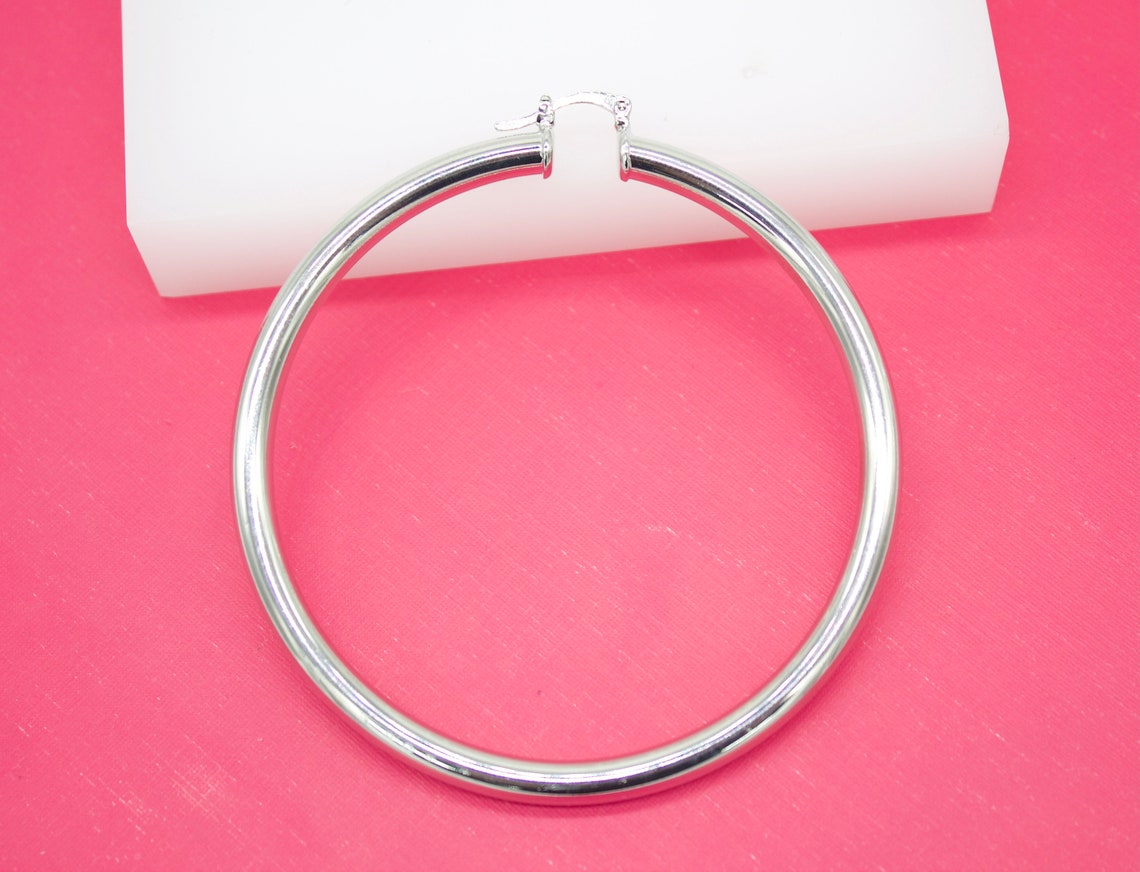 A large, polished silver hoop earring rests against a vibrant pink background.