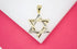 A two-tone gold and silver Star of David pendant rests on a white display surface against a bright pink background.