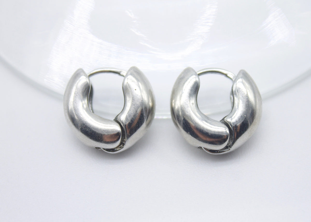 A pair of polished silver chunky hoop earrings rest side by side on a clean white surface.