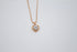 A delicate rose gold heart necklace features a brilliant crystal gemstone pendant suspended from a fine chain against a light background.
