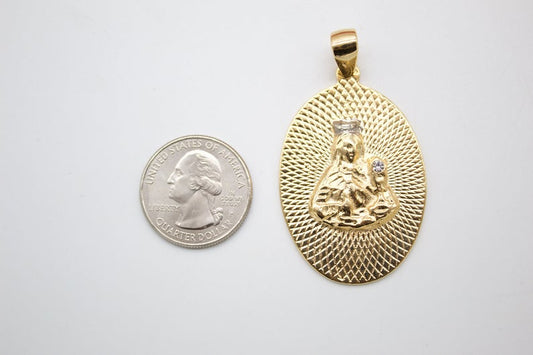 A gold oval pendant featuring Our Lady of Guadalupe rests beside a US quarter coin for scale.