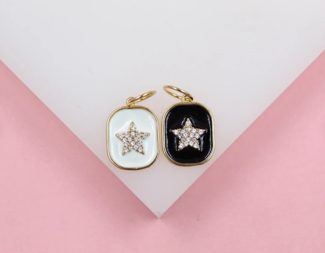 Two gold-framed enamel star pendants, one white and one black, rest on a white display surface.