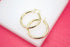 A pair of polished gold hoop earrings rests gracefully on a white display stand against a vibrant pink backdrop.