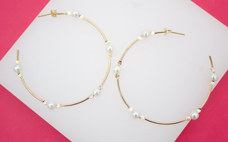 A pair of elegant gold hoop earrings accented with delicate white pearls and sparkling rhinestones rests on a display surface.