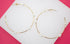 A pair of elegant gold hoop earrings accented with delicate white pearls and sparkling rhinestones rests on a display surface.