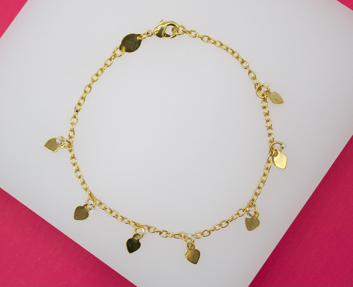 A delicate gold chain bracelet features hanging heart charms displayed on a white and pink background.