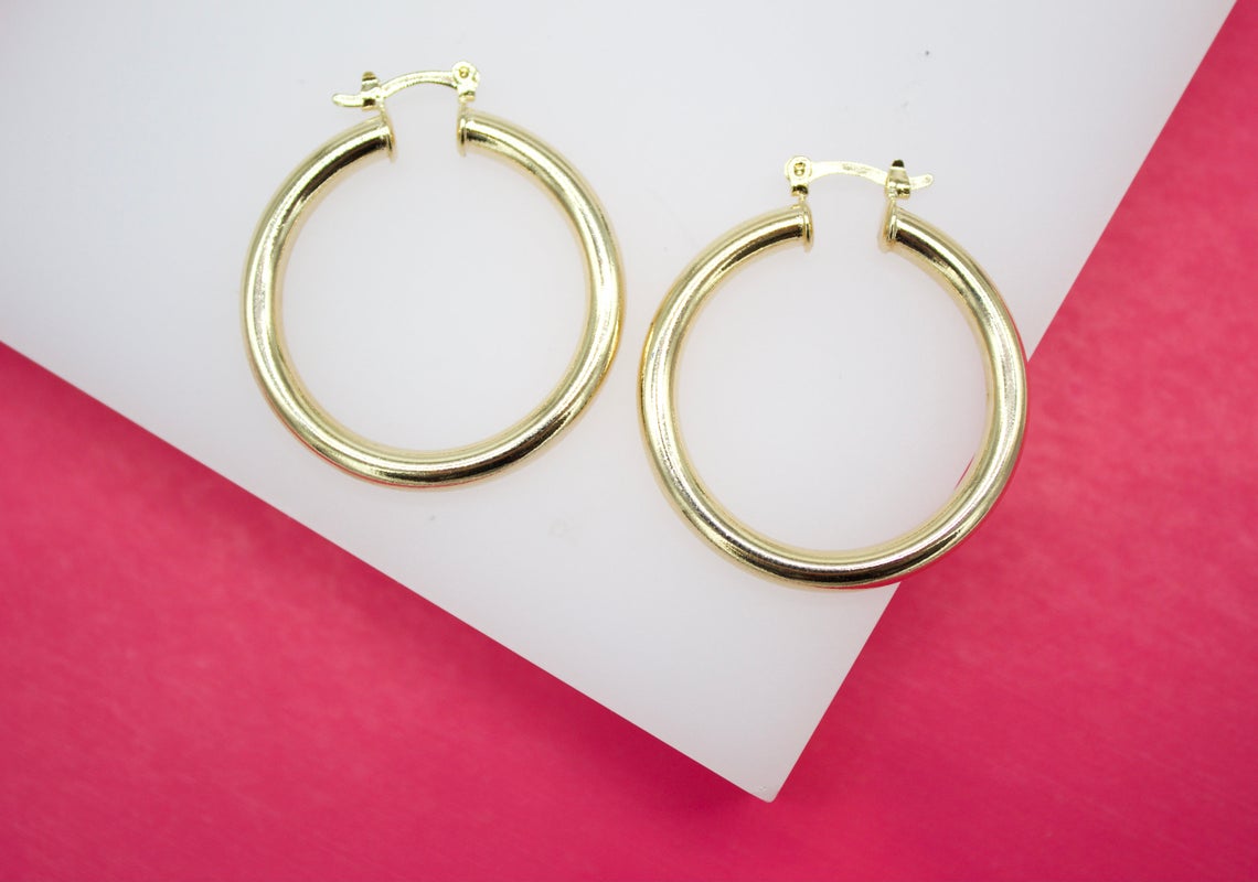 A pair of classic gold hoop earrings rests neatly on a white surface against a bright pink background.