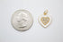 A gold-plated white enamel heart charm featuring a paved cubic zirconia center rests next to a US quarter coin for scale.